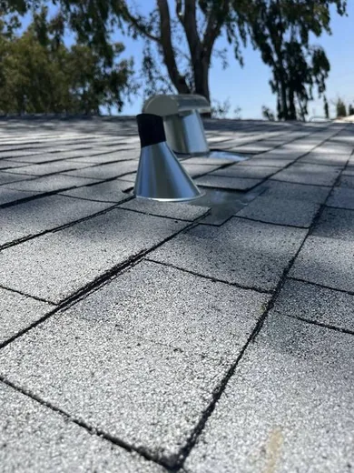 Close-up of a new metal pipe flashing boot set into a freshly laid asphalt shingle roof