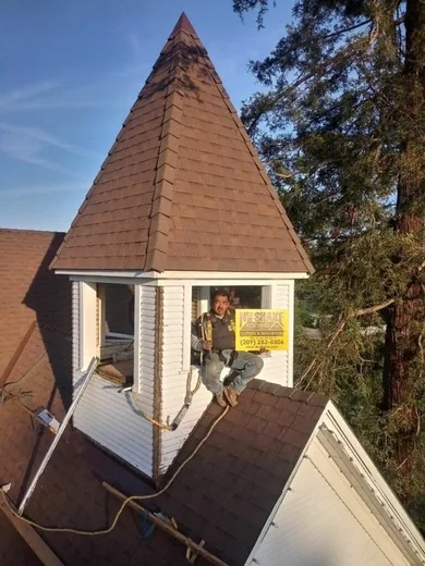 NuShake roofer in a safety harness leaning from the window of a steep turret finished with wood shake roofing